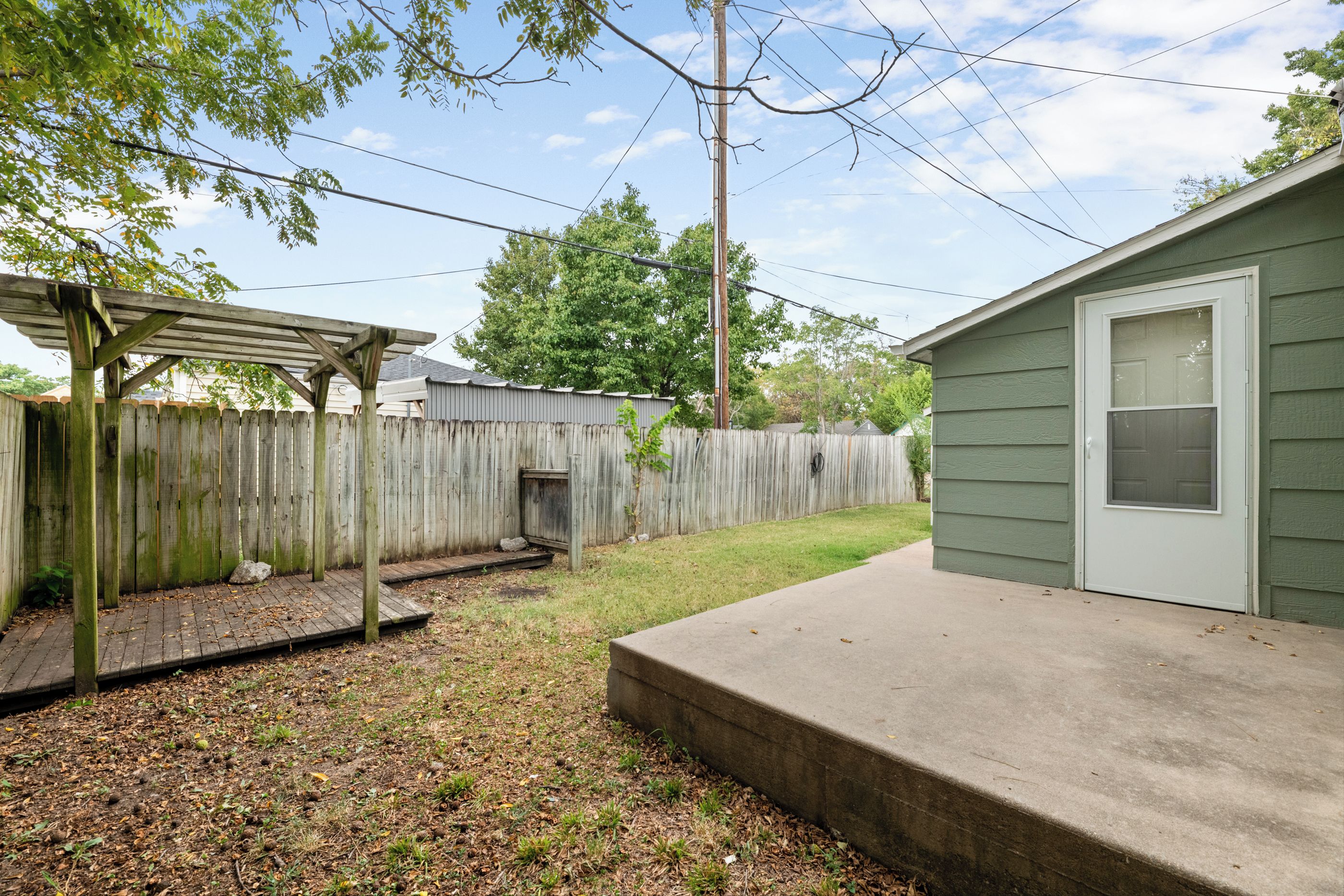 A residential backyard with a wooden deck, a concrete patio, and a metal fence.