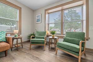 A room with two green armchairs, a wooden table, and a lamp. There is a window with blinds and a picture on the wall. - Easy Access to US-54 | Fenced Yard + W/D | Perfect for Travel Nurses! (Wichita)