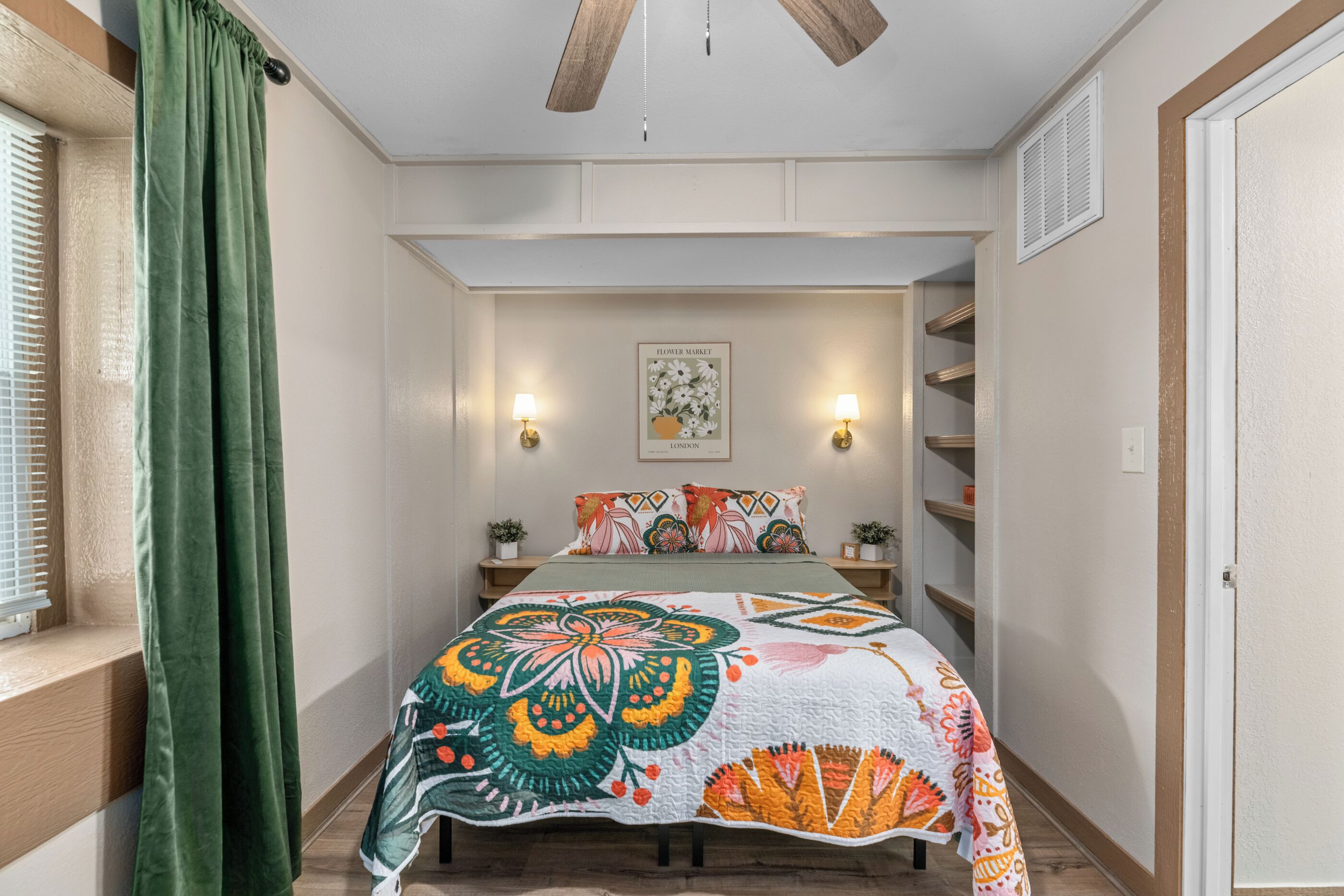 Un dormitorio con una cama, una ventana con persianas, una cortina verde, una lámpara de pared y un cuadro enmarcado.