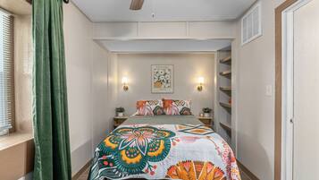 Un dormitorio con una cama, una ventana con persianas, una cortina verde, una lámpara de pared y un cuadro enmarcado.