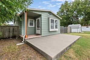 A small, single-story house with a front porch, a visible door, and a small window. - Easy Access to US-54 | Fenced Yard + W/D | Perfect for Travel Nurses! (Wichita)