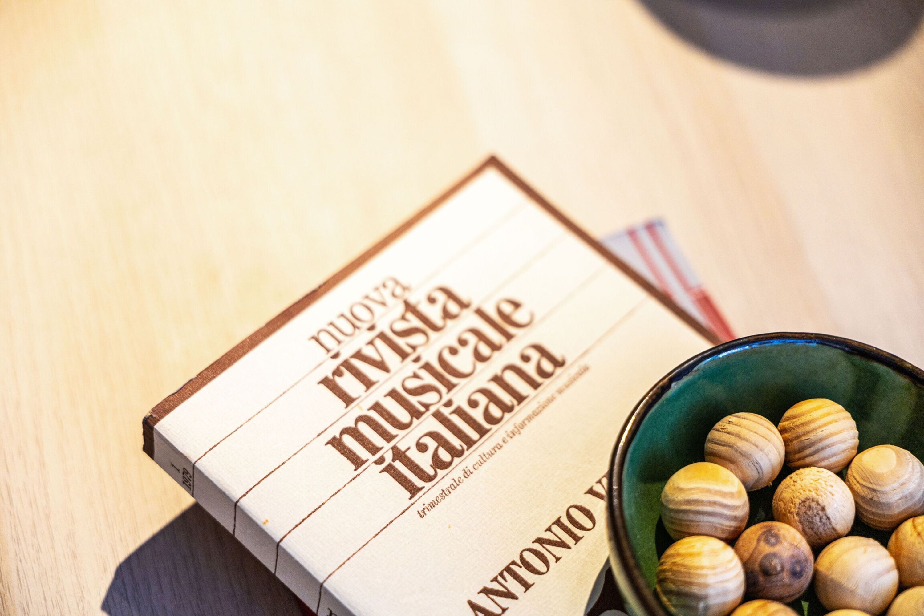 Um livro intitulado 'Nuova rivista musicale italiana' e uma tigela com objetos redondos e texturizados.
