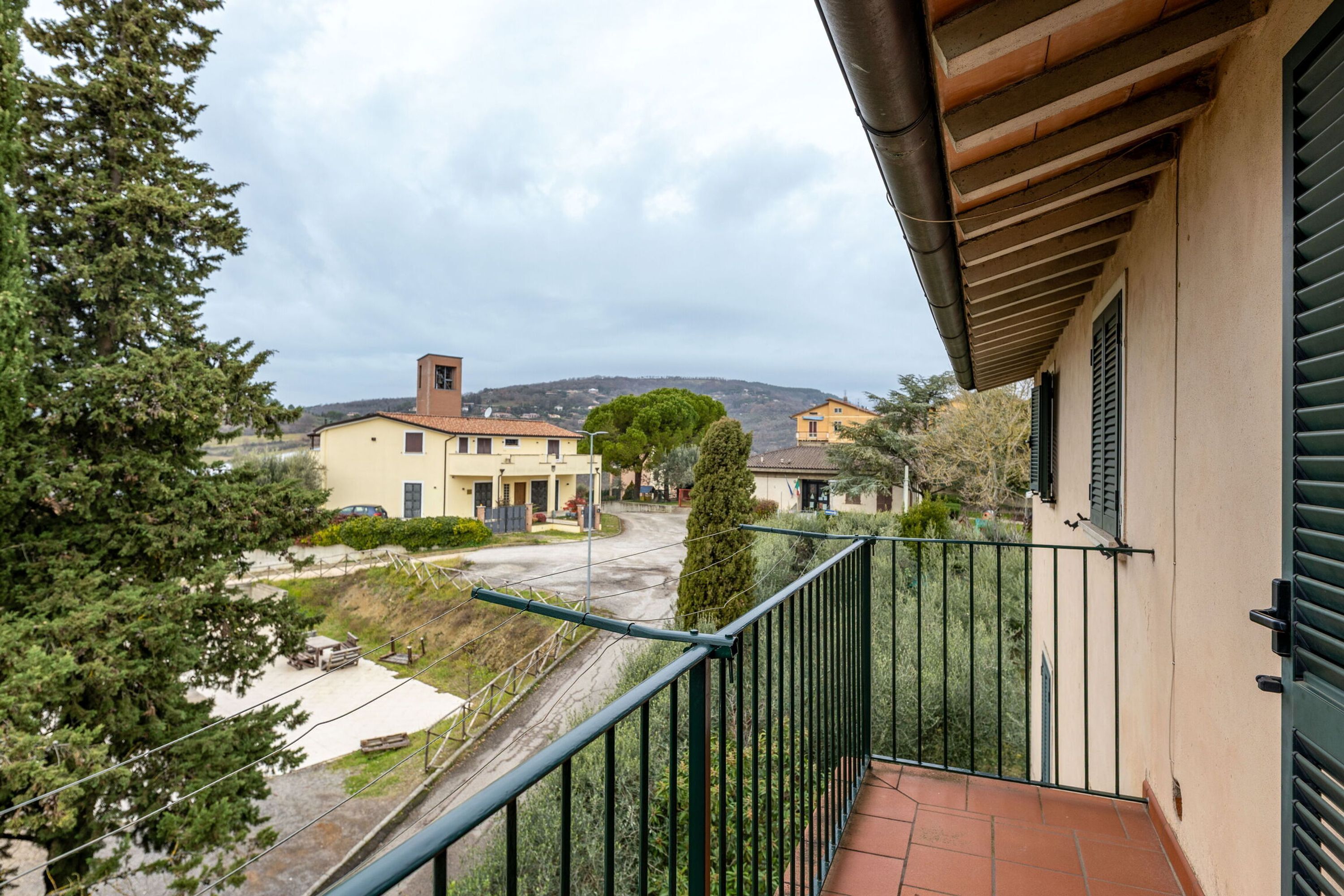A residential balcony with a view of a street, houses, and trees.