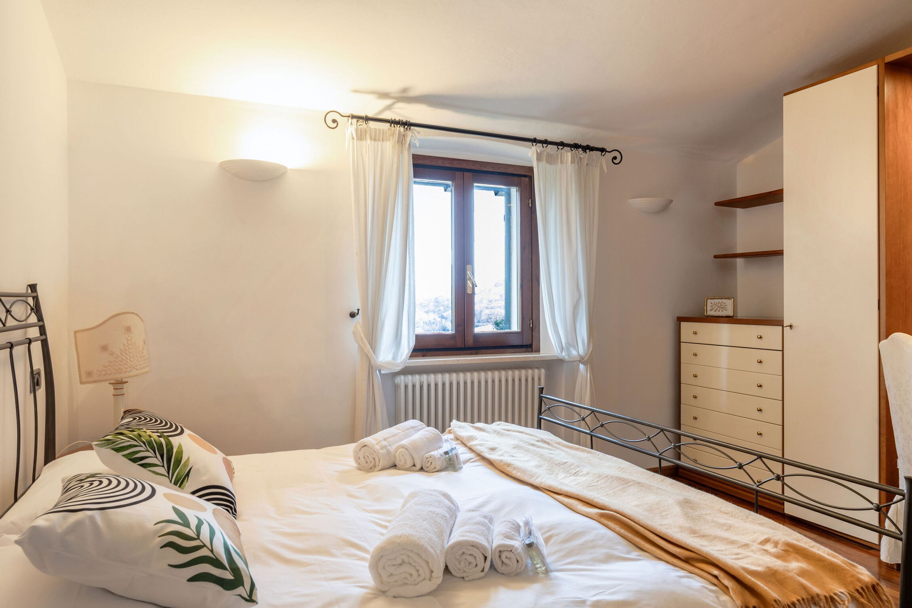 Una camera da letto con un letto, un termosifone, una finestra con tende, un comodino e un armadio.
