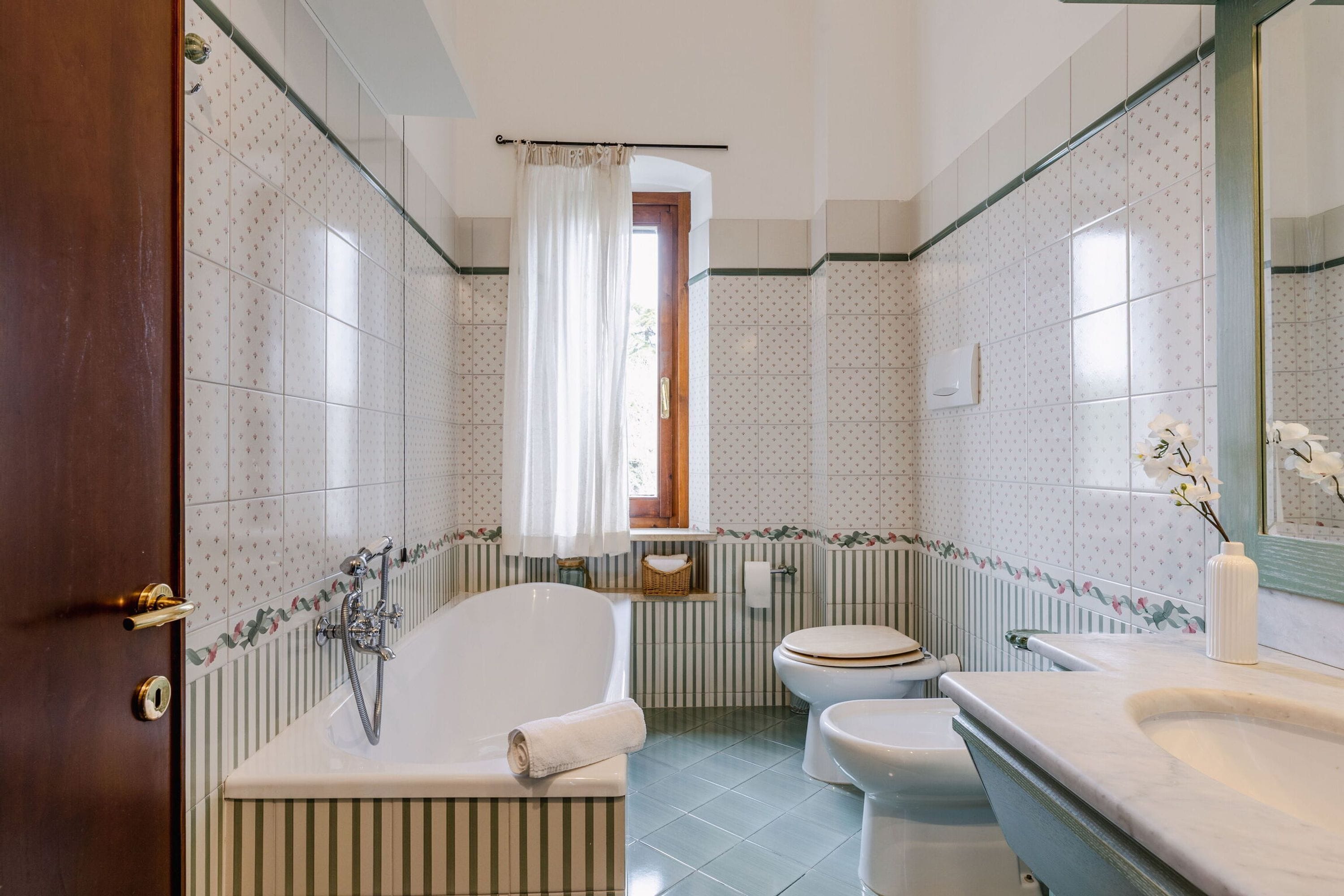 A bathroom with a bathtub, toilet, and sink, featuring striped and floral patterned tiles.