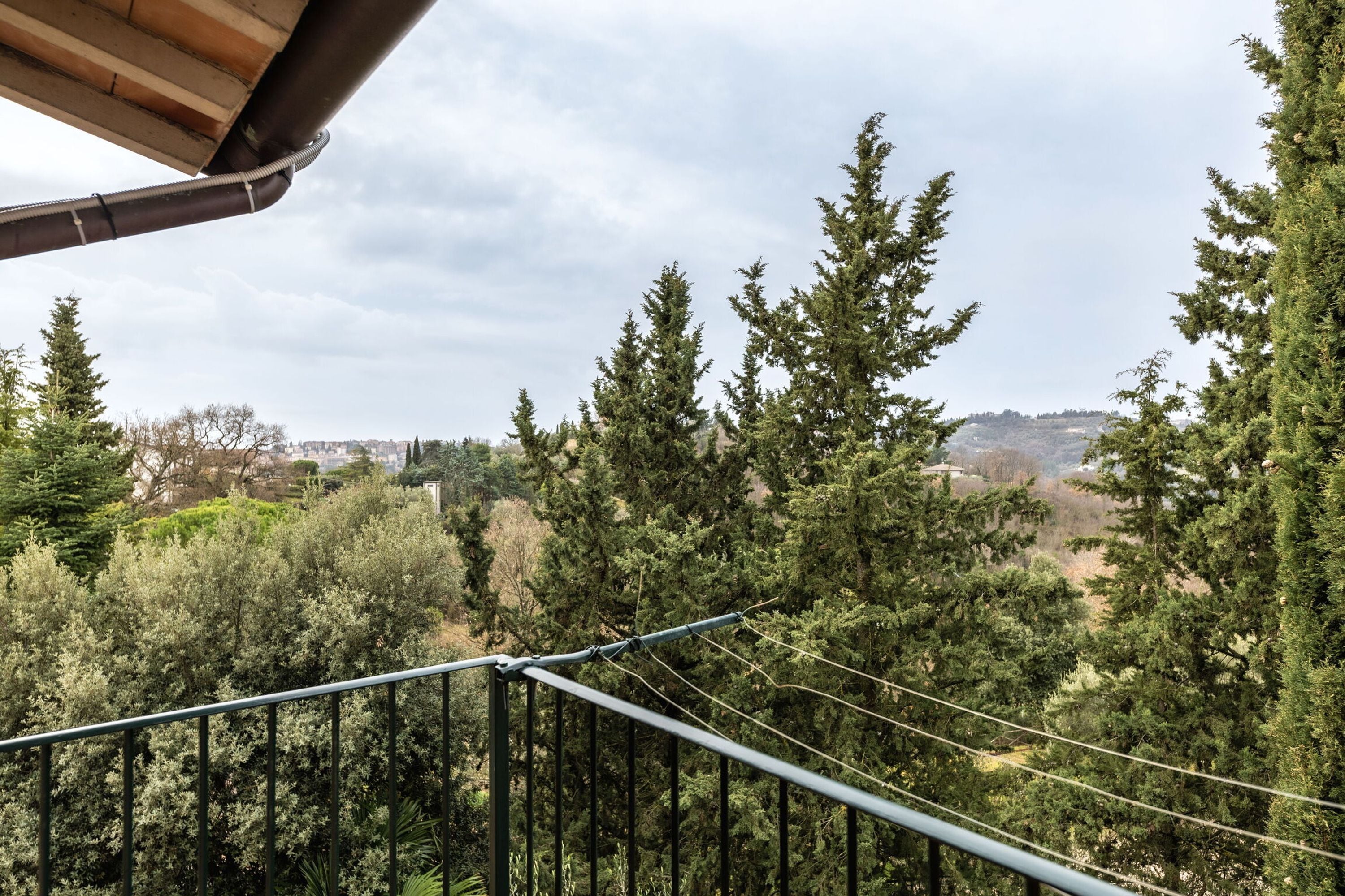 A balcony with a view of a forested area and a distant cityscape.
