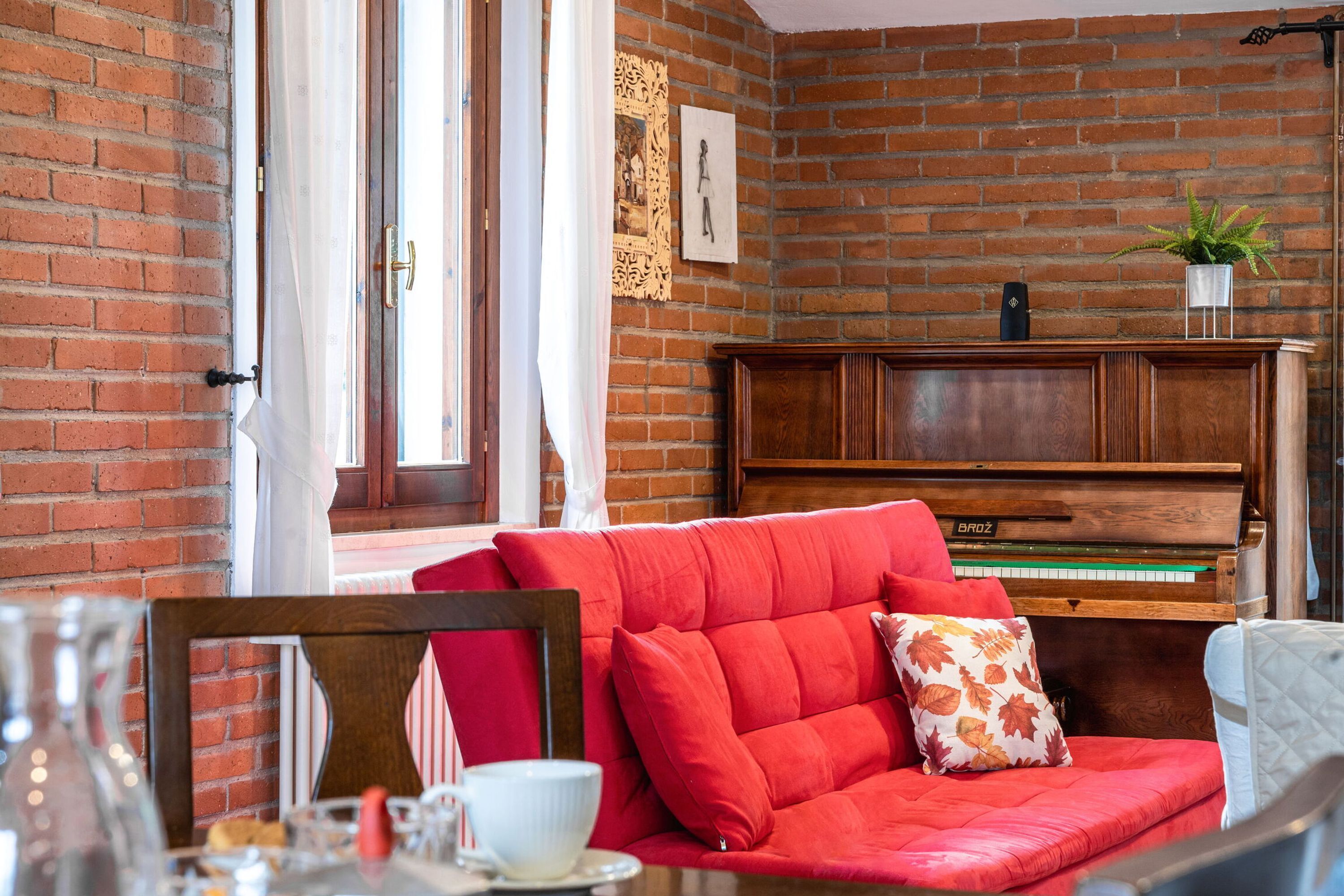 Un soggiorno accogliente con un divano rosso, un pianoforte in legno e un muro in mattoni.