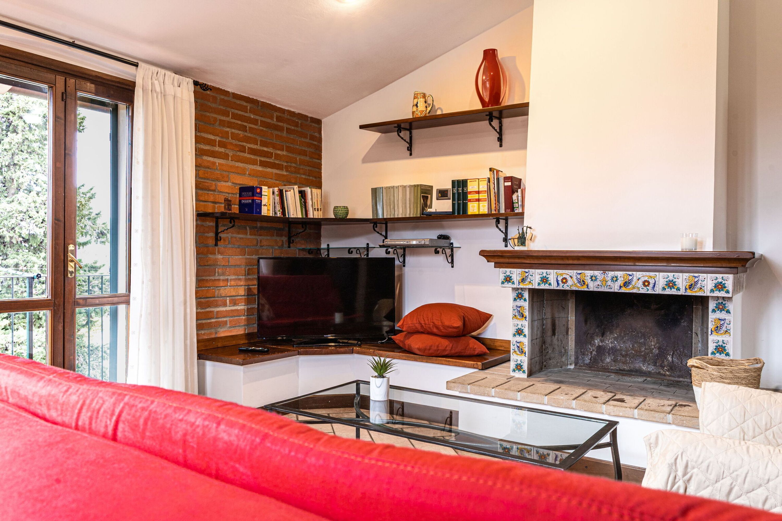 A cozy living room with a fireplace, bookshelves, and a red sofa.