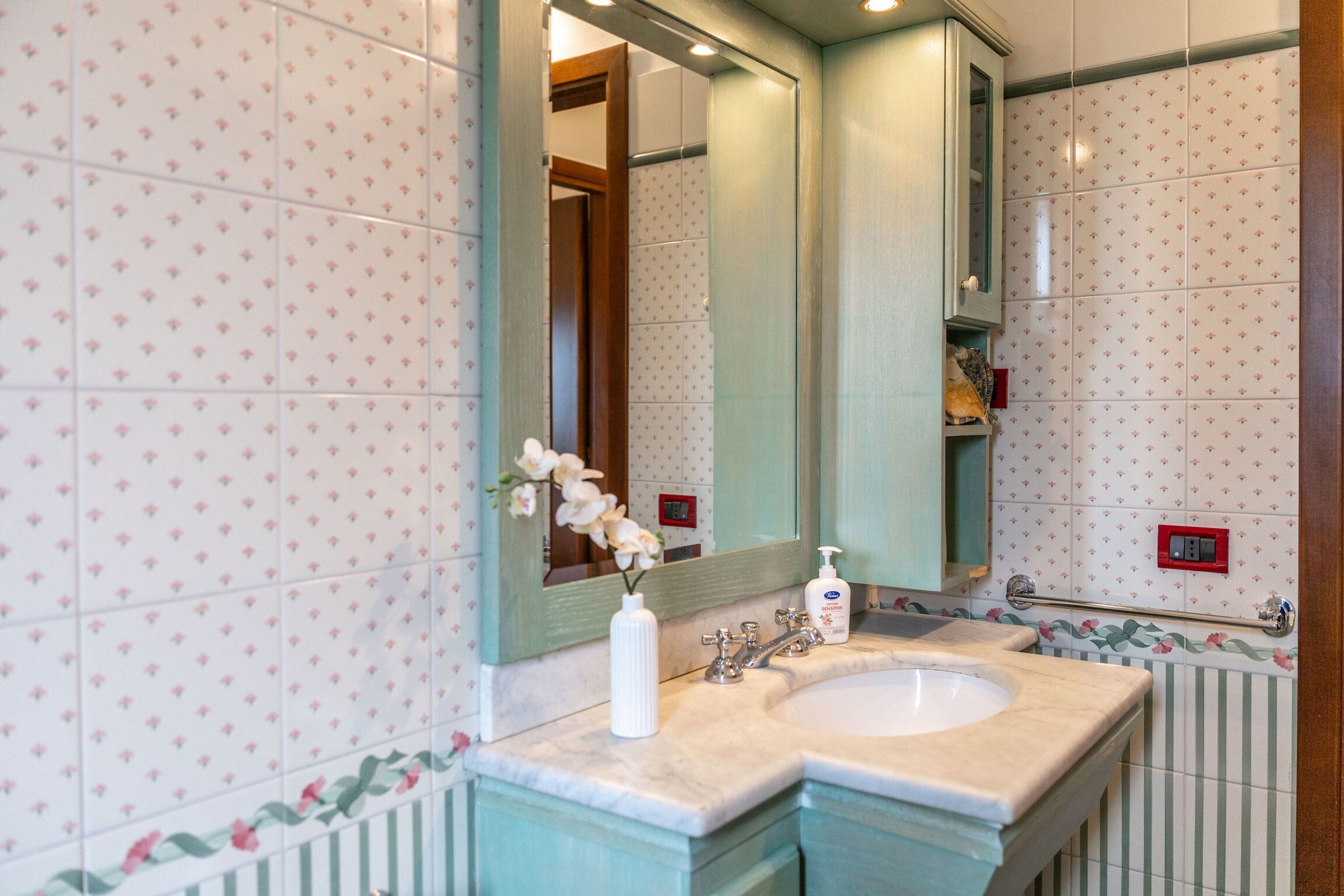 A bathroom with a double sink, a large mirror, and floral-patterned tiles.