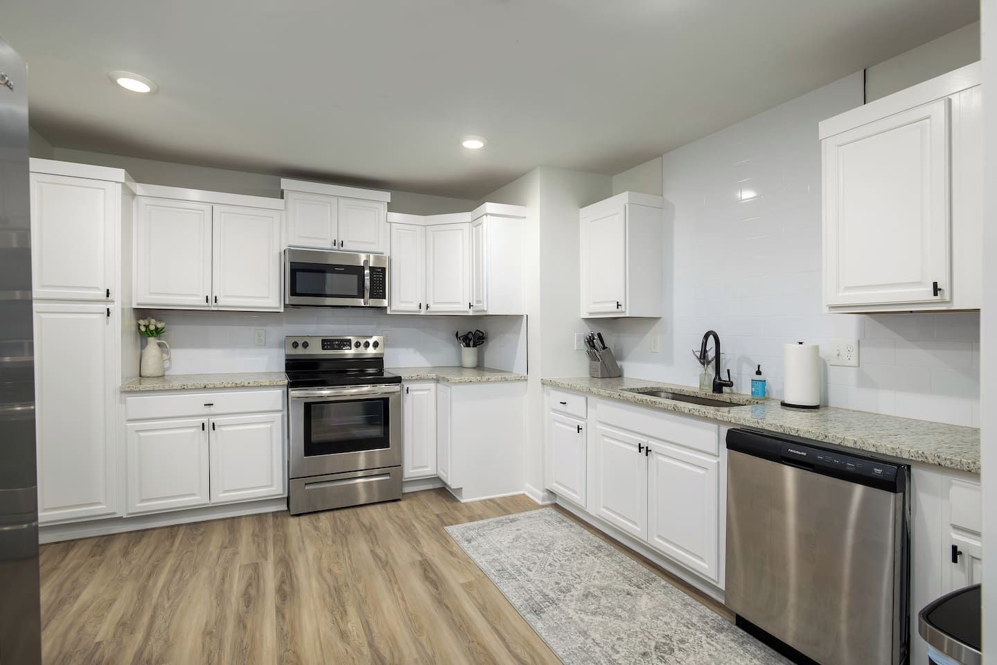 Una cocina moderna con muebles blancos, electrodomésticos de acero inoxidable y encimera de granito.