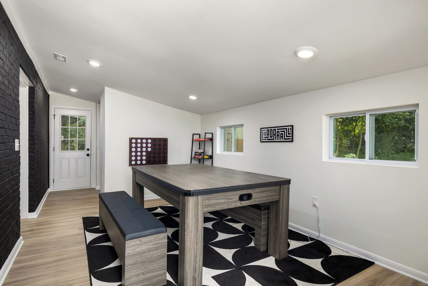 Una cocina moderna con una mesa de madera y un banco, un tapete a cuadrícula blanco y negro, una puerta con ventana y un estante en la pared con objetos.