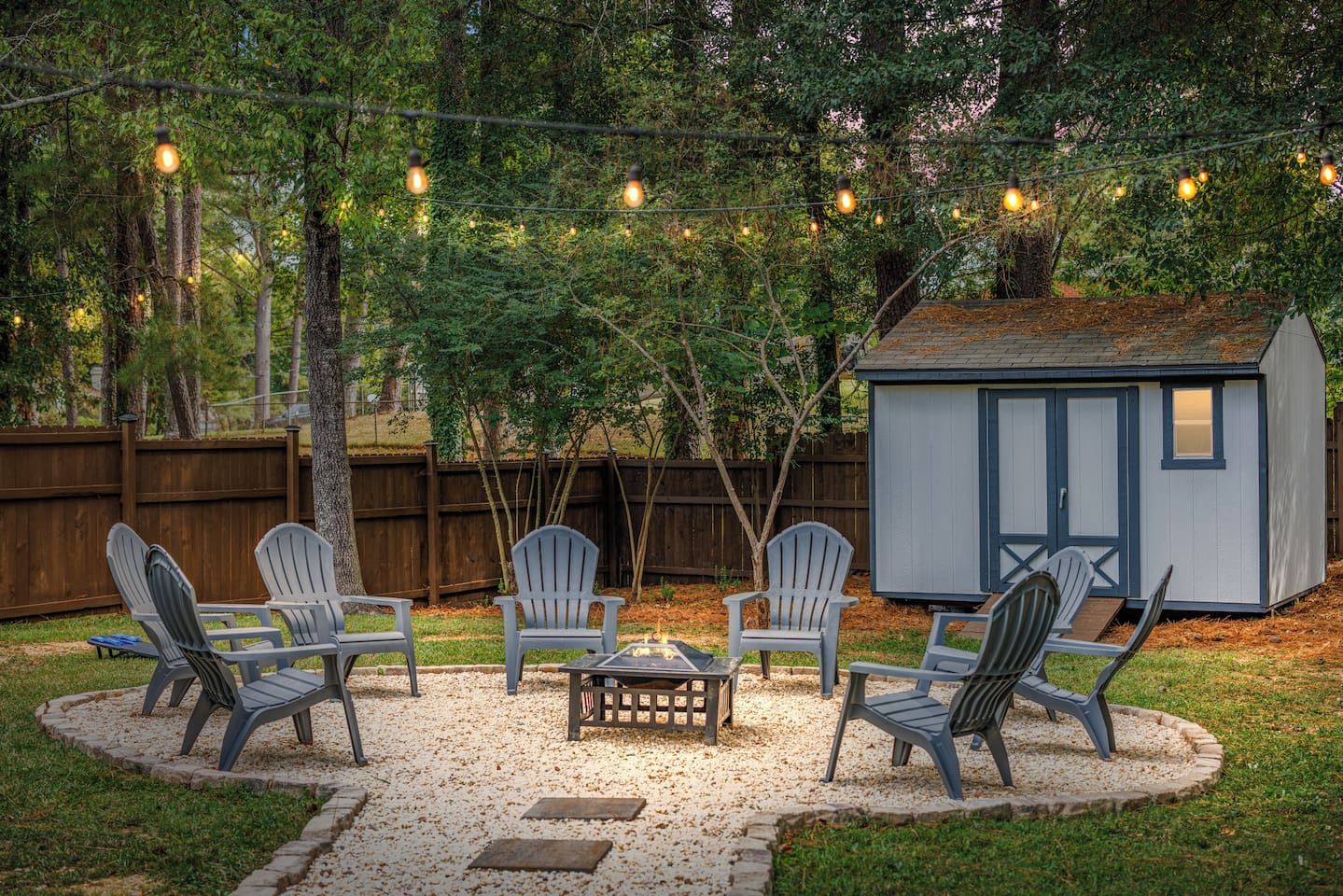 A backyard with a fire pit, Adirondack chairs, and a shed.