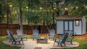 A backyard with a fire pit, Adirondack chairs, and a shed.