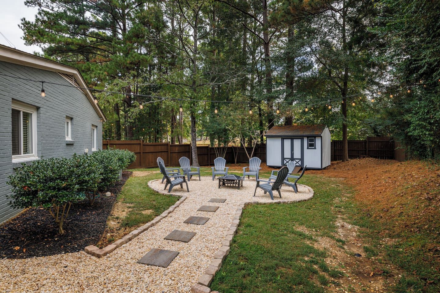 Ein Garten mit einer Terrassenfläche, Sitzgelegenheiten im Freien und einem kleinen Gartenhaus.
