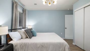 Un dormitorio con cama, lámparas de noche, una ventana con cortinas, una puerta y un candelabro.