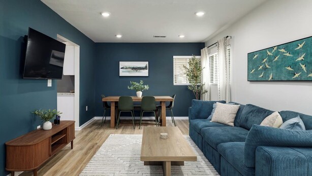 Ein modernes Wohnzimmer mit blauer Wand, einem Holzesstisch, einem blauen Sofa und einem flachbildfernseher an der Wand.