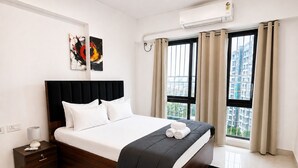Quarto de hotel moderno com uma cama grande, mesa de cabeceira, cortinas e ar condicionado.