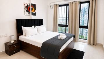 A modern hotel room with a large bed, a bedside table, a nightstand, a window with curtains, and an air conditioning unit.