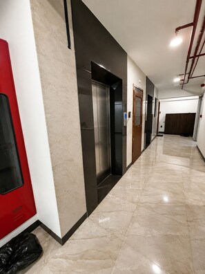 Un pasillo con una puerta roja, un ascensor negro y un cubo de basura.