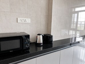 A kitchen with a black microwave, a silver electric kettle, and a black toaster on a black countertop. - Premium 2-bedroom apartment in santacruz the heart of Mumbai (Mumbai)