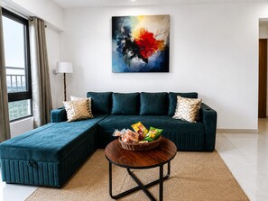 Un salon moderne avec un canapé d’angle, une table basse ronde et un tableau abstrait aux couleurs vives accroché au mur.
