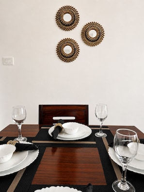 Una mesa de comedor lista con platos, fuentes y vasos blancos, junto a una silla de madera oscura.