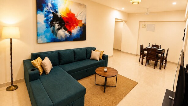 Uma sala de estar com sofá modular, mesa de centro, mesa de jantar com cadeiras e televisão de tela plana.
