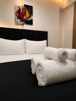 Una habitación de hotel con cabecera negra, ropa de cama blanca y un cuadro en la pared.