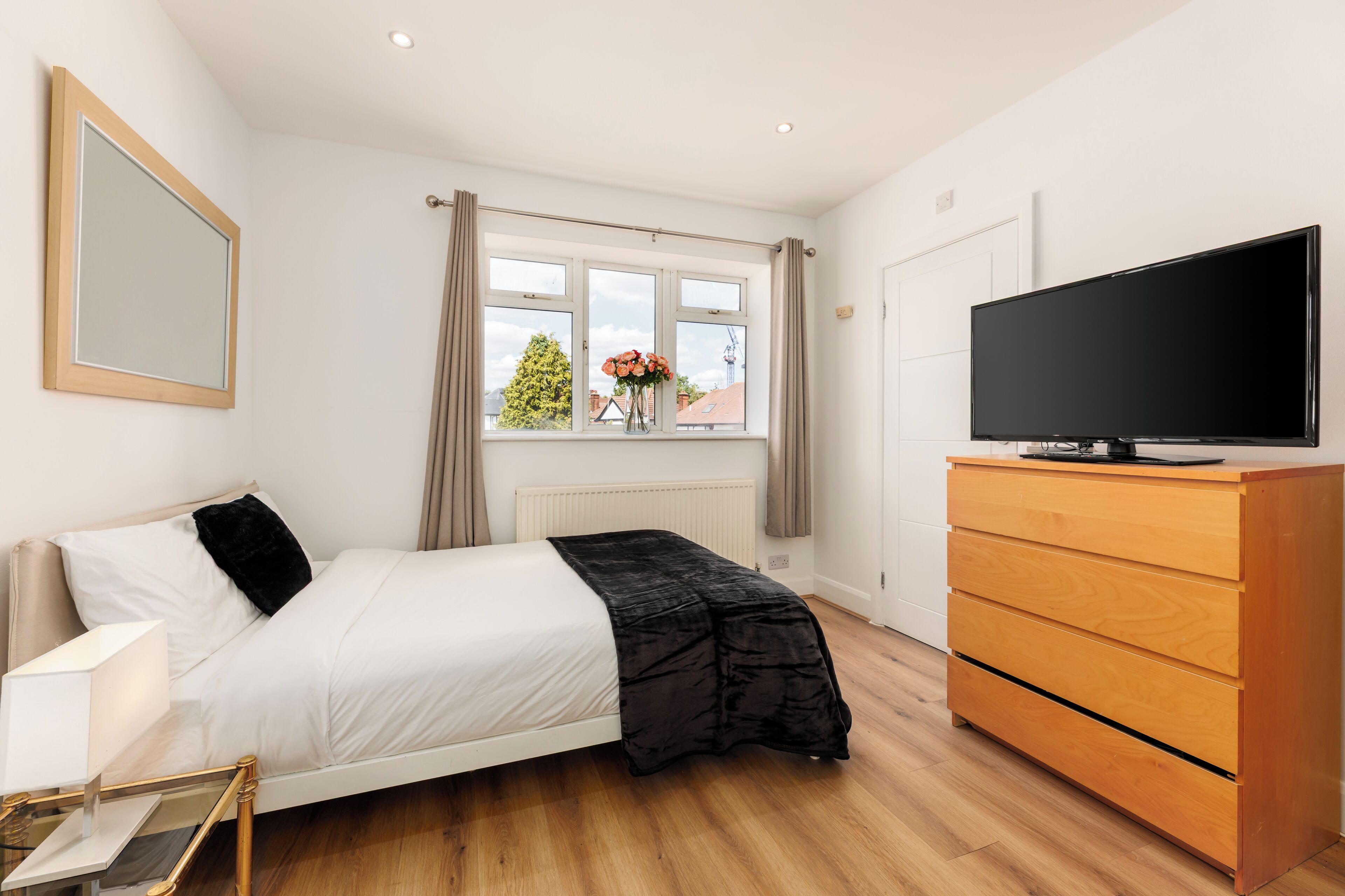 Une chambre à coucher avec un lit, une commode, un téléviseur et une fenêtre avec des rideaux.