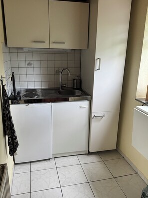Una cocina compacta con armarios blancos, un lavamanos de acero inoxidable y un salpicadero de azulejos.
