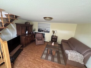 Una sala de estar con escalera de madera, un sofá, una mesa de centro y un televisor.