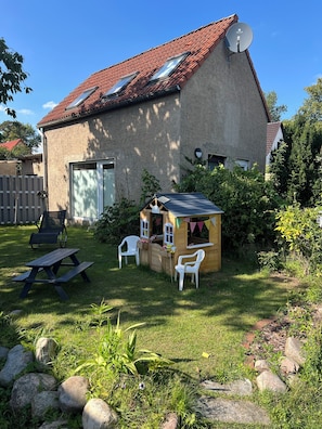 A house with a sloped roof, a satellite dish, a wooden playhouse, and a picnic table. - Cozy vacation home on two floors. Just 3 minutes to Lake Neukloster (Neukloster)