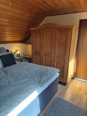 A bedroom with a bed, wooden wardrobe, and a nightstand with a lamp. - Cozy vacation home on two floors. Just 3 minutes to Lake Neukloster (Neukloster)