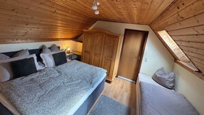 A bedroom with a wooden ceiling, a bed with multiple pillows, a desk with a lamp, and a wardrobe. - Cozy vacation home on two floors. Just 3 minutes to Lake Neukloster (Neukloster)