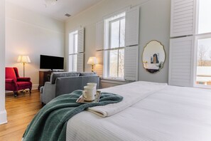 A hotel room with a bed, a television, a red chair, and two lamps. - Spacious Historic King Room by New River Trail (Max Meadows)