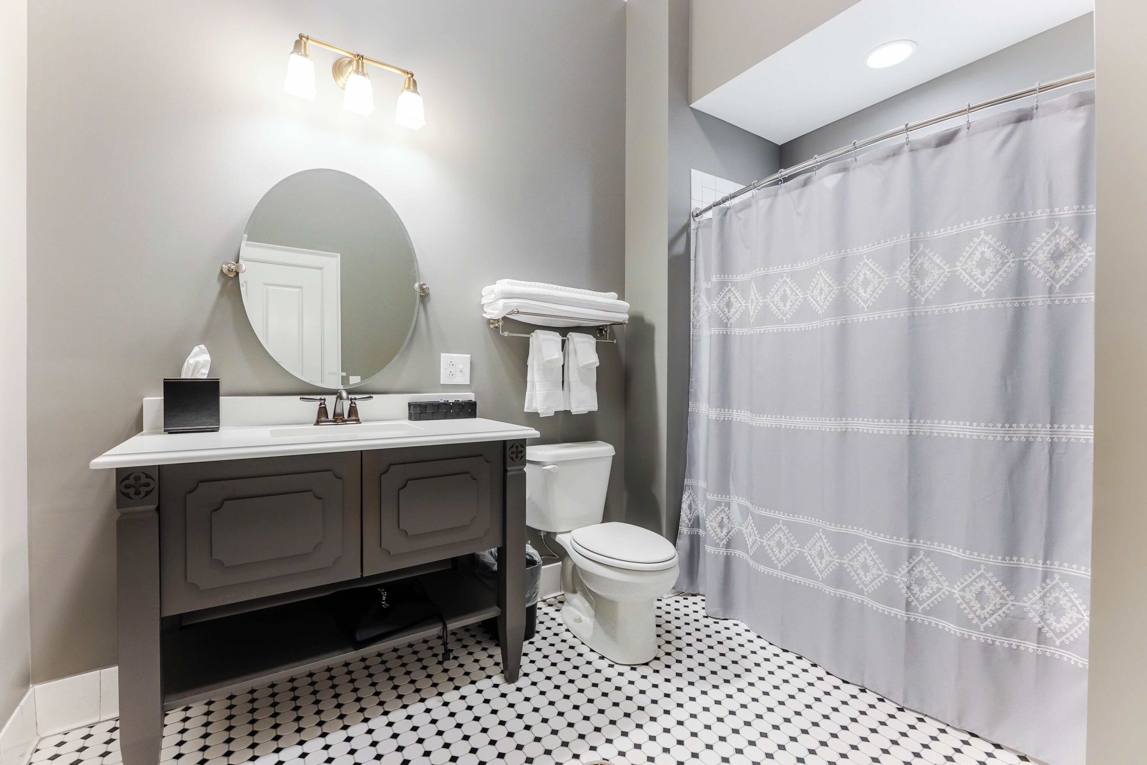 A bathroom with a round mirror, a sink with a towel rack, a toilet, and a shower curtain.
