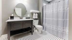 A bathroom with a round mirror, a sink with a towel rack, a toilet, and a shower curtain.
