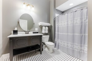 A bathroom with a round mirror, a sink with a towel rack, a toilet, and a shower curtain. - Spacious Historic King Room by New River Trail (Max Meadows)