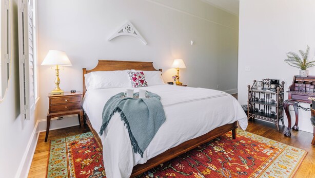 A neatly made bed with two bedside lamps, a decorative wall piece, and a coffee station with a plant.