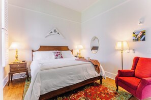 A neatly arranged bedroom with a wooden bed, two bedside tables with lamps, a red chair, a mirror, and a wall-mounted artwork. - Spacious Historic King Room by New River Trail (Max Meadows)
