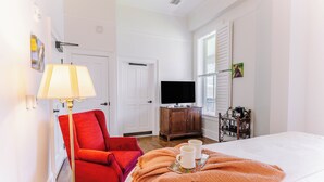 Une chambre d’hôtel avec un lit, un fauteuil rouge, une télévision, une armoire en bois et une fenêtre avec des volets.