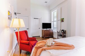 A hotel room with a bed, a red armchair, a television, a wooden cabinet, and a window with shutters. - Spacious Historic King Room by New River Trail (Max Meadows)