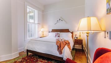 A bedroom with a bed, bedside lamps, a nightstand, a red chair, and a window with shutters.