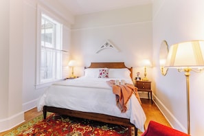 A neatly arranged bedroom with a bed, bedside tables, lamps, and a window. - Spacious Historic King Room by New River Trail (Max Meadows)