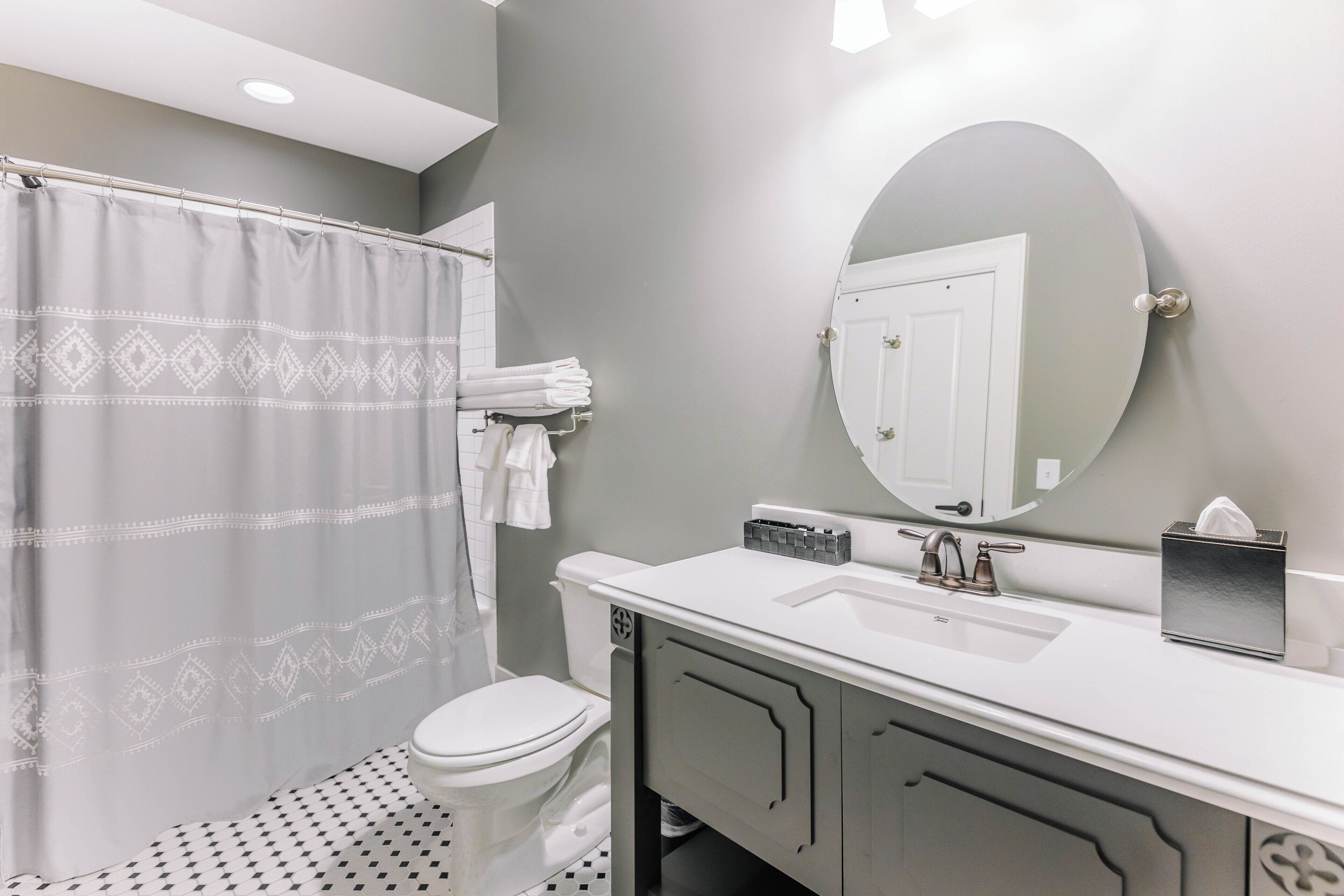 A bathroom with a shower curtain, a toilet, a sink with a mirror, and a towel rack.