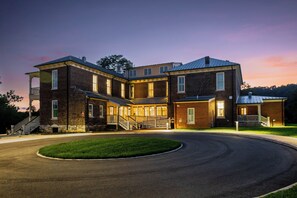 A large, multi-story brick building with a central courtyard, a covered staircase, and a well-lit entrance. - Cozy Historic Inn Room by New River Trail (Max Meadows)