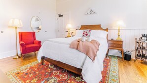 A neatly arranged bedroom with a single bed, a red armchair, two bedside tables with lamps, and a patterned rug. - First-Floor Queen Room with Mountain Views (Max Meadows)