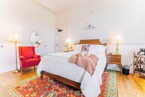 A neatly arranged bedroom with a single bed, a red armchair, two bedside tables with lamps, and a patterned rug. - First-Floor Queen Room with Mountain Views (Max Meadows)