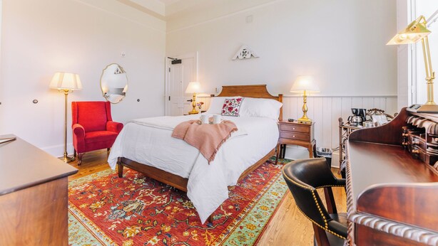 A hotel room with a bed, two bedside tables, a desk, a chair, a red armchair, and a patterned rug. - First-Floor Queen Room with Mountain Views (Max Meadows)