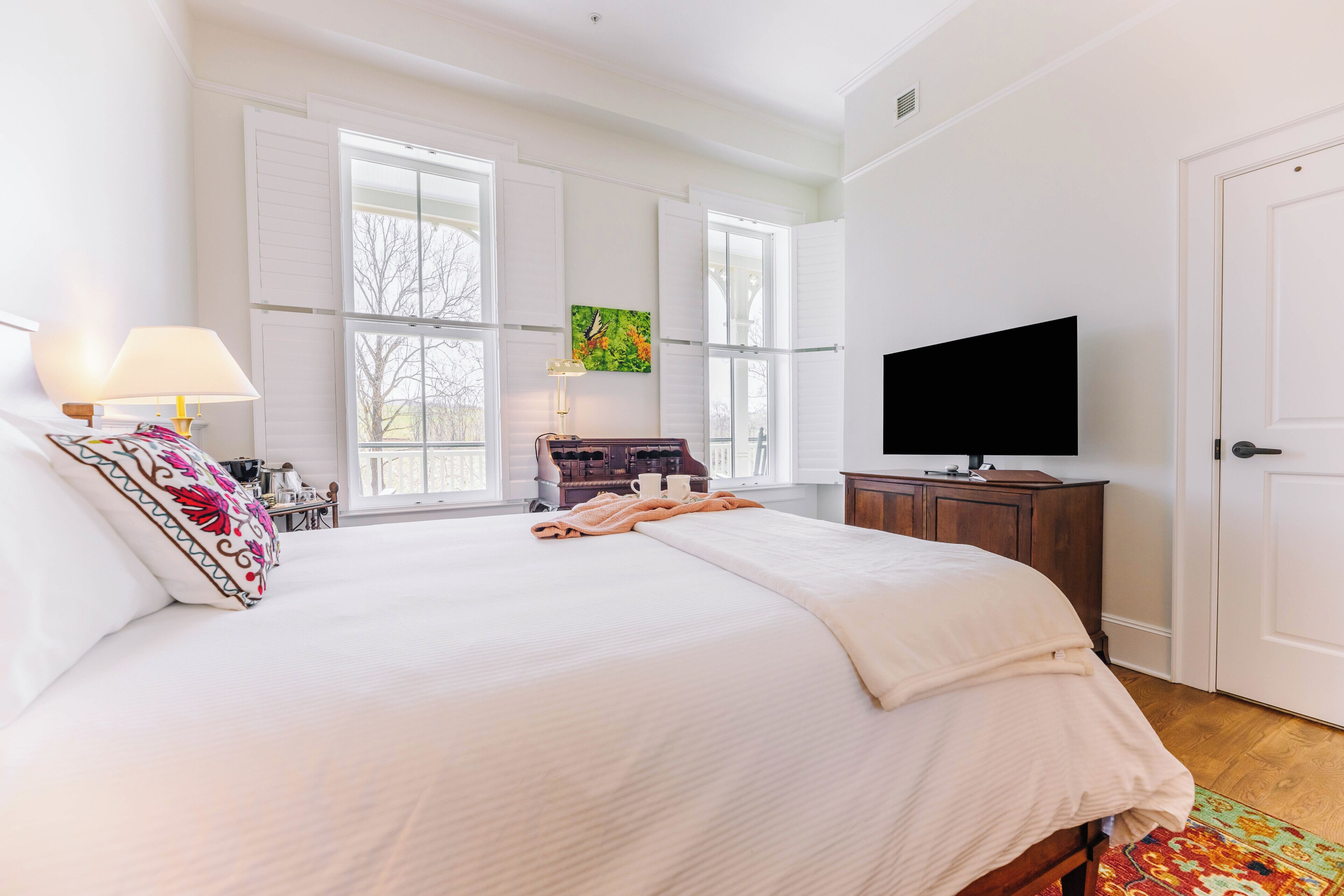 A bedroom with a large bed, a television, a desk with a lamp, and a window with a butterfly painting.